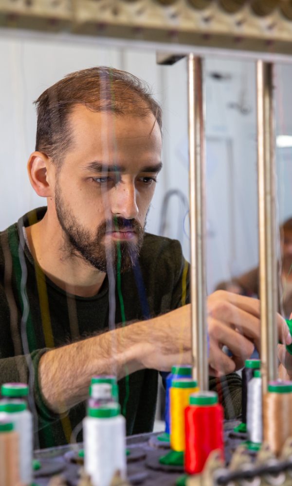 Young worker changing a spool from an industrial embroidery machine. Bobine multicolore